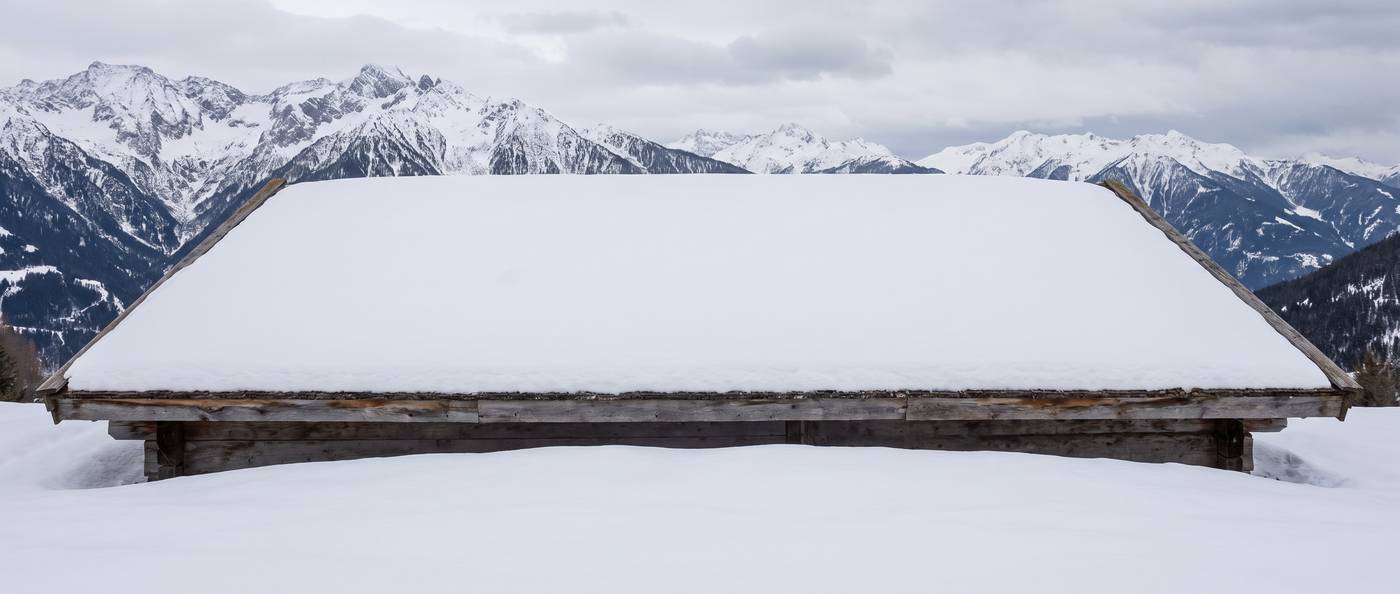 A broad low-slope roof section of a mountain home buried under deep settled snow