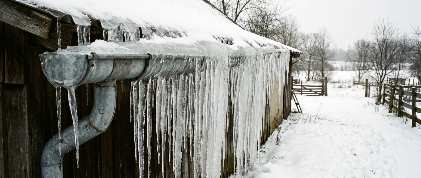A gutter packed solid with ice and a dense curtain of icicles below a snowy roof edge