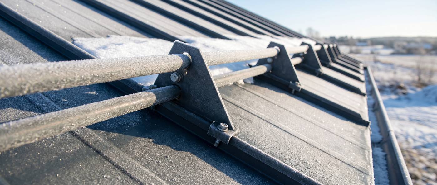 Close detail of metal snow guards clamped to the raised seams of a dark standing-seam metal roof